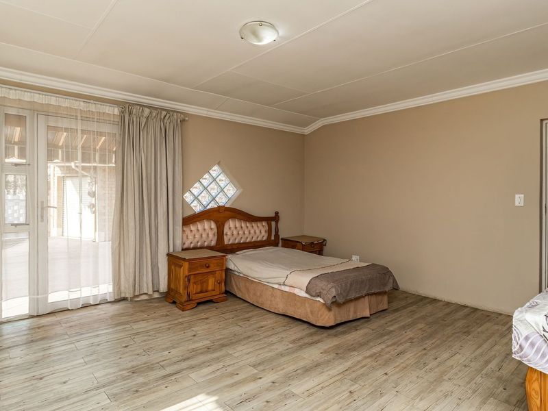 Spacious bedroom featuring wood-look laminate flooring, a unique diamond-shaped glass block window, and direct access to the exterior via a glass sliding door.