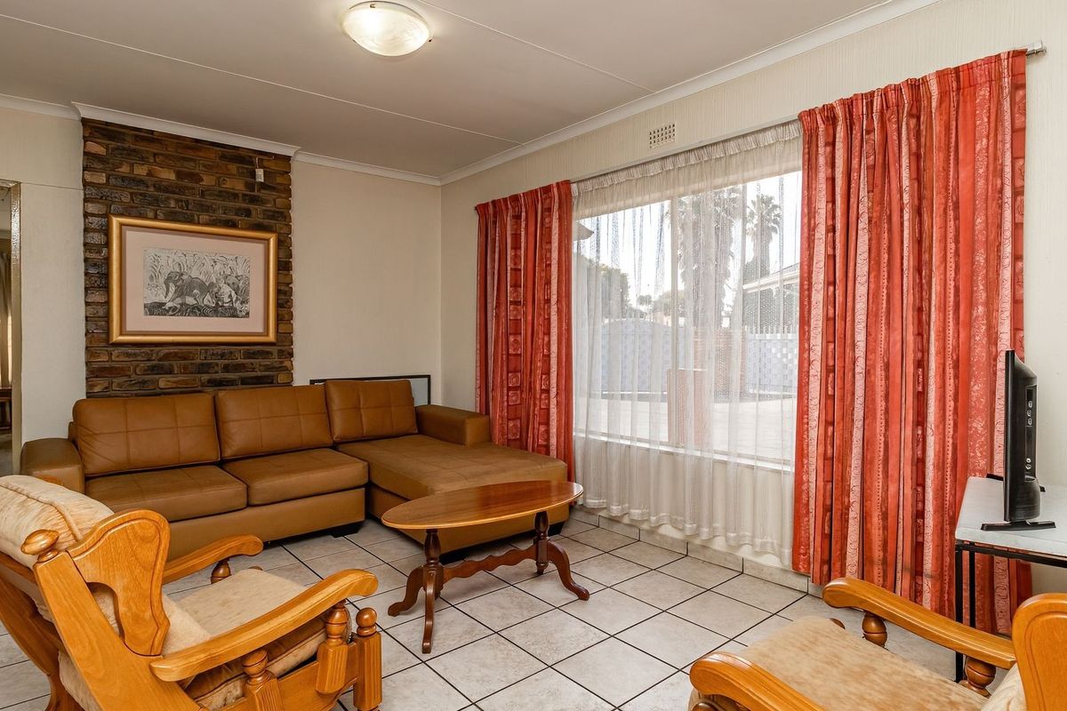 A living room featuring a brick fireplace, tiled flooring, and large windows with curtains, offering a functional and traditional living space.