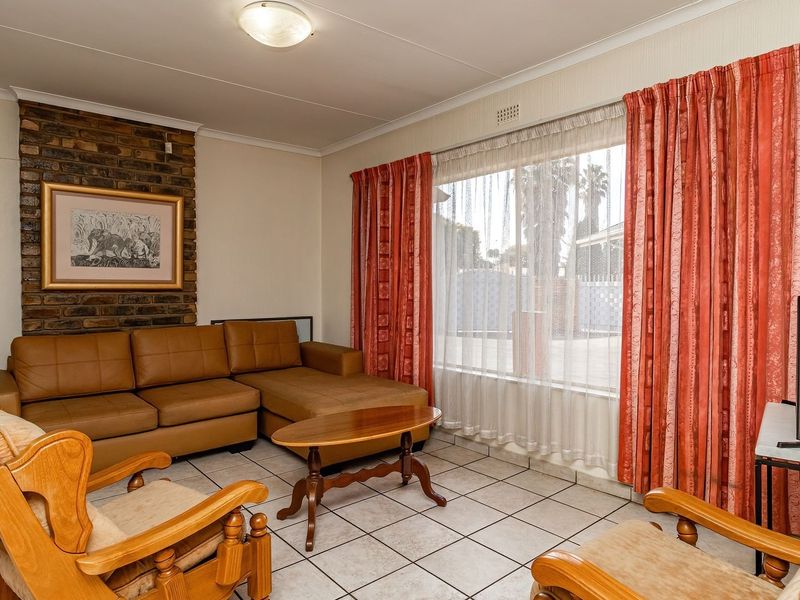 A living room featuring a brick fireplace, tiled flooring, and large windows with curtains, offering a functional and traditional living space.