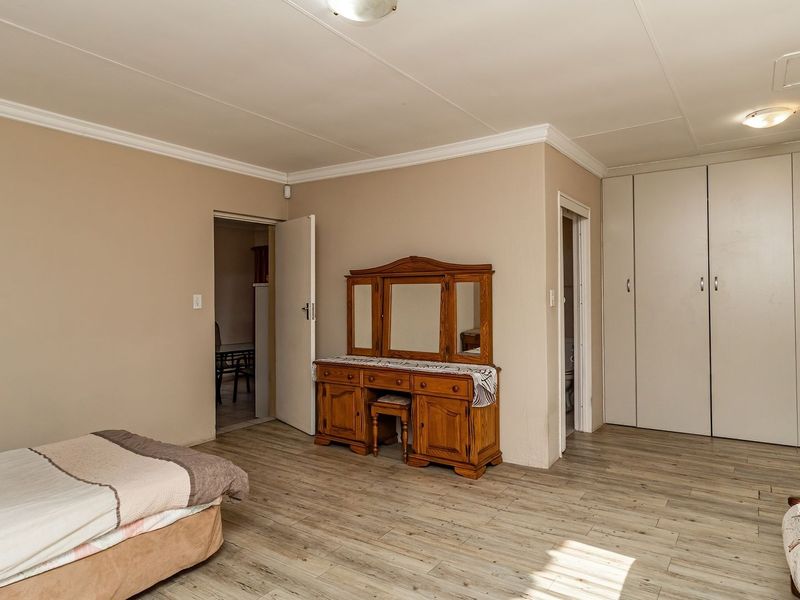 Spacious bedroom featuring light-toned laminate flooring, neutral wall finishes, and extensive built-in cupboard storage.