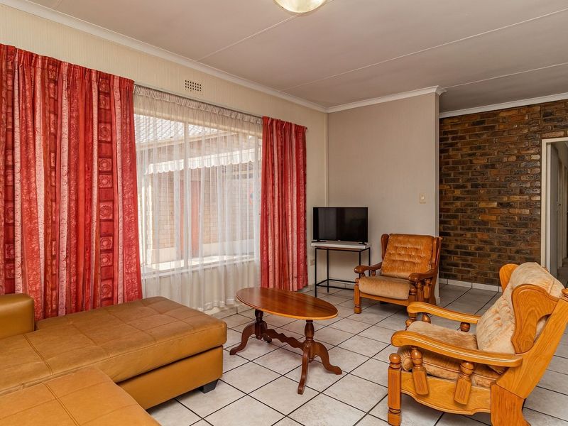 A living room featuring ceramic floor tiles, an exposed brick feature wall, and a coved ceiling, providing a functional and dated living space.