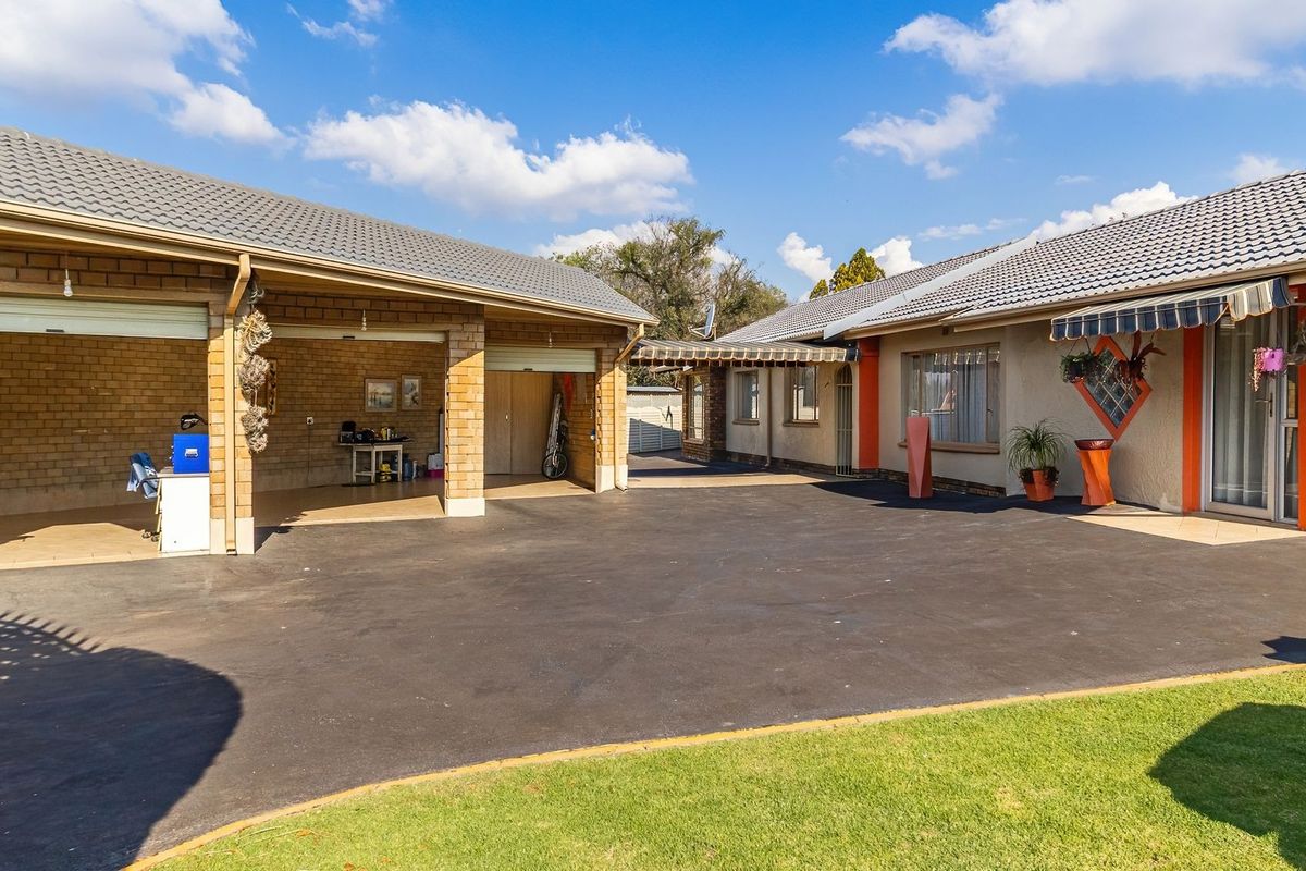 Spacious rear exterior area featuring a large asphalt driveway, a multi-car garage, and a covered patio section with retractable awnings.