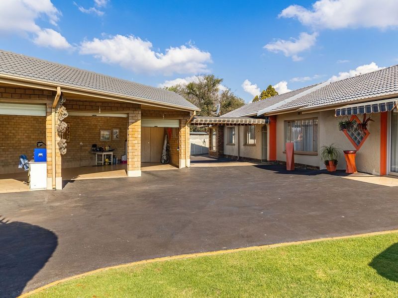 Spacious rear exterior area featuring a large asphalt driveway, a multi-car garage, and a covered patio section with retractable awnings.