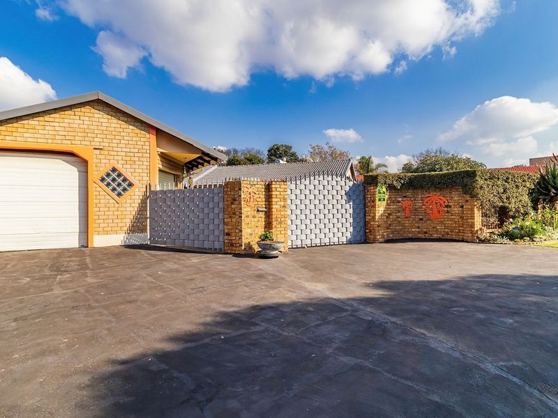 Front exterior view of the property featuring a brick facade, a single garage, and a paved driveway with secure boundary walling.