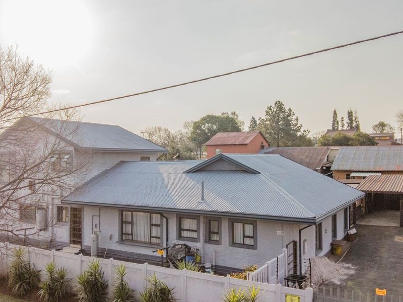 Aerial view of the property showing the main house with a corrugated metal roof, paved driveway, carport, and perimeter boundary wall.