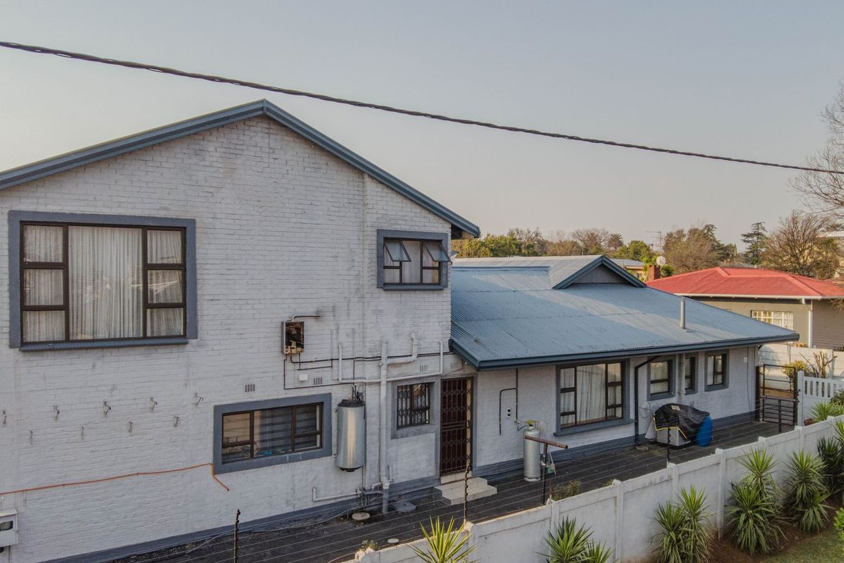 Aerial view of the rear elevation featuring painted brick walls, corrugated metal roofing, and a secure boundary wall.