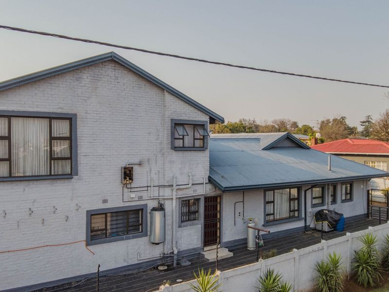 Aerial view of the rear elevation featuring painted brick walls, corrugated metal roofing, and a secure boundary wall.