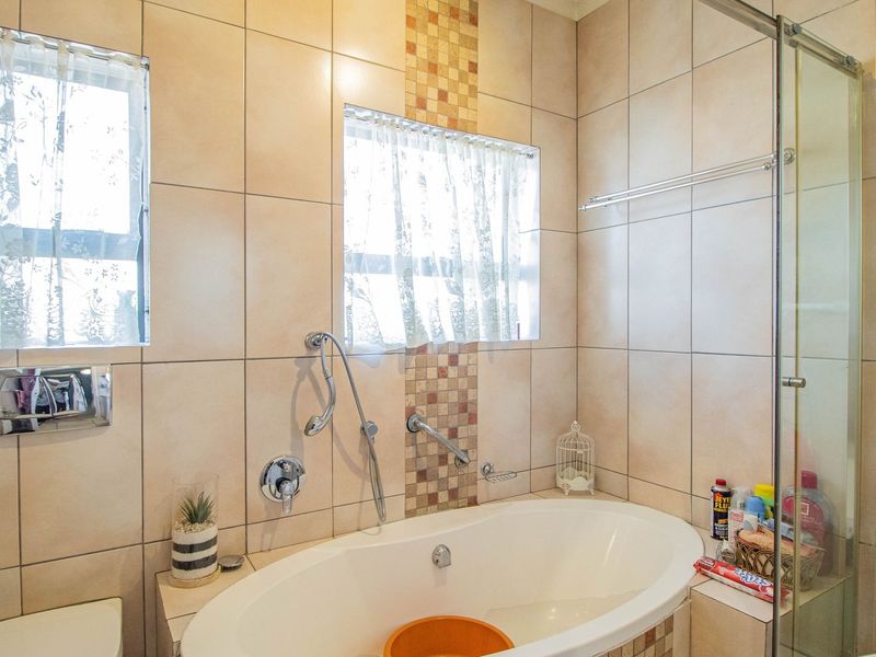 A functional bathroom featuring a built-in bathtub, a separate glass-enclosed shower, and neutral ceramic wall tiling with a decorative mosaic accent.