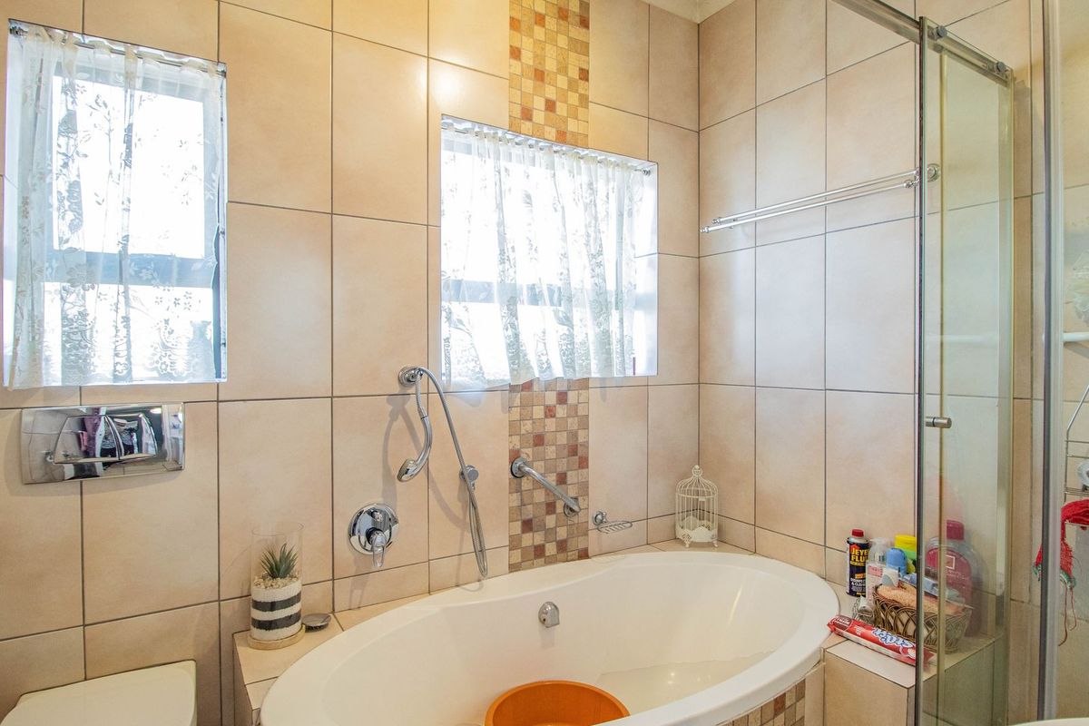 A functional bathroom featuring a built-in bathtub, a separate glass-enclosed shower, and neutral ceramic wall tiling with a decorative mosaic accent.