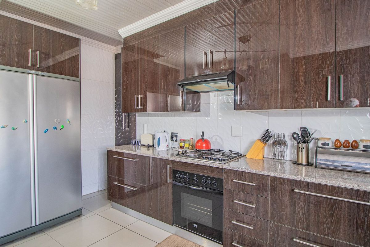 Modern kitchen featuring dark wood-grain cabinetry, granite countertops, a gas hob, built-in oven, and a tiled backsplash.