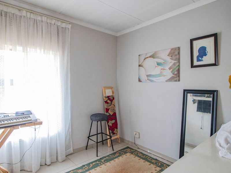 A bedroom featuring tiled flooring and natural light from a window with curtain rails.