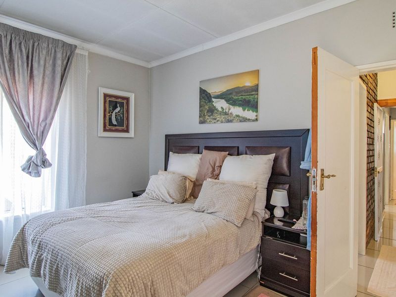 A well-lit bedroom featuring tiled flooring and neutral wall tones, with an open doorway leading to an adjacent hallway and bathroom area.
