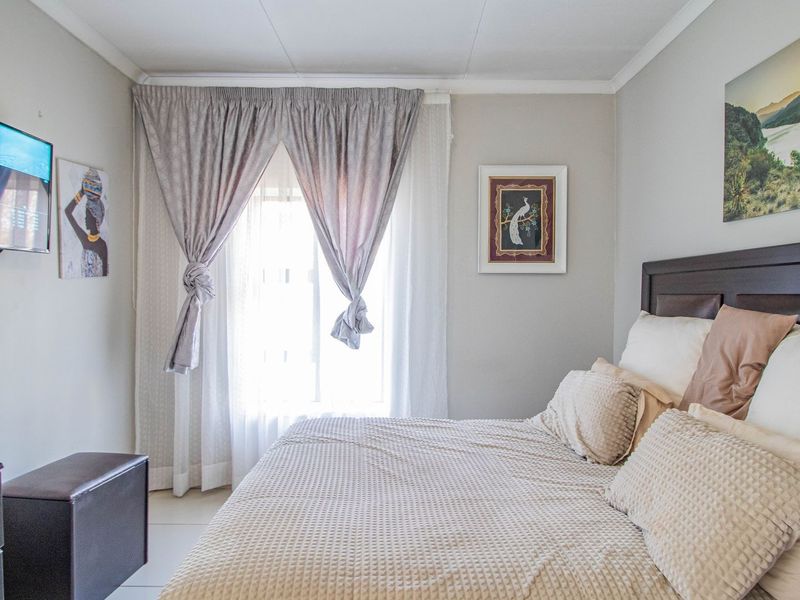 A well-lit bedroom featuring neutral wall tones, tiled flooring, and window treatments, providing a comfortable and functional sleeping space.