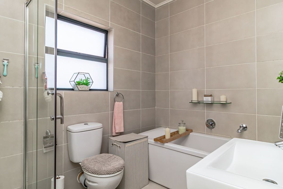 A modern bathroom featuring a glass-enclosed shower, a bathtub with wall-mounted fixtures, a basin, and neutral wall tiling.