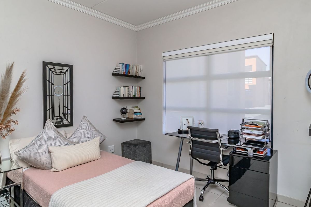 A well-maintained bedroom featuring neutral walls, coving, built-in shelving, and a large window with a roller blind.