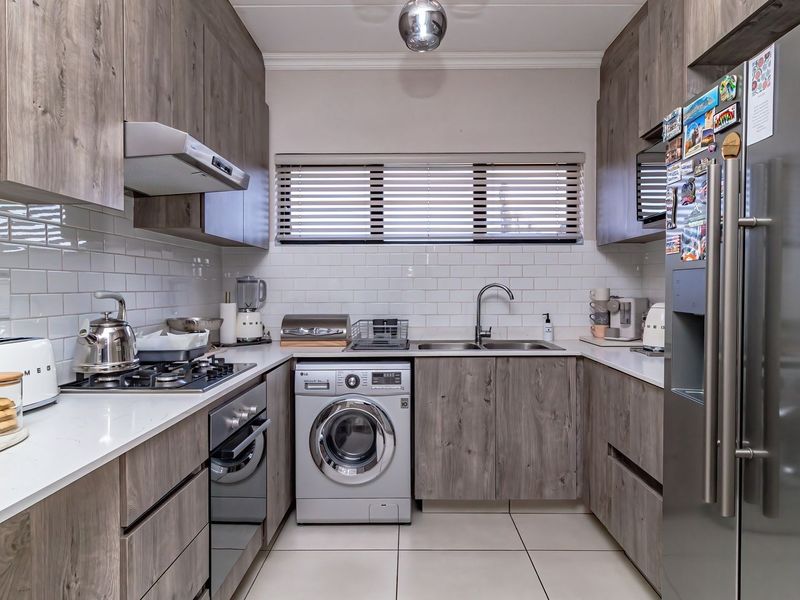 Modern galley-style kitchen featuring wood-grain cabinetry, quartz countertops, subway tile backsplash, built-in gas hob, oven, and integrated laundry appliance.