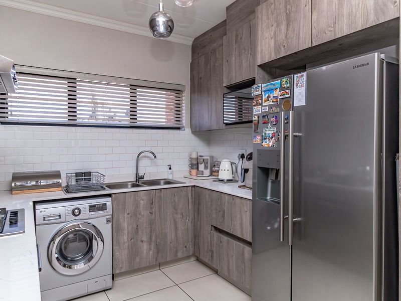Modern kitchen featuring wood-grain cabinetry, subway tile backsplash, gas hob with extractor, and integrated space for a washing machine.