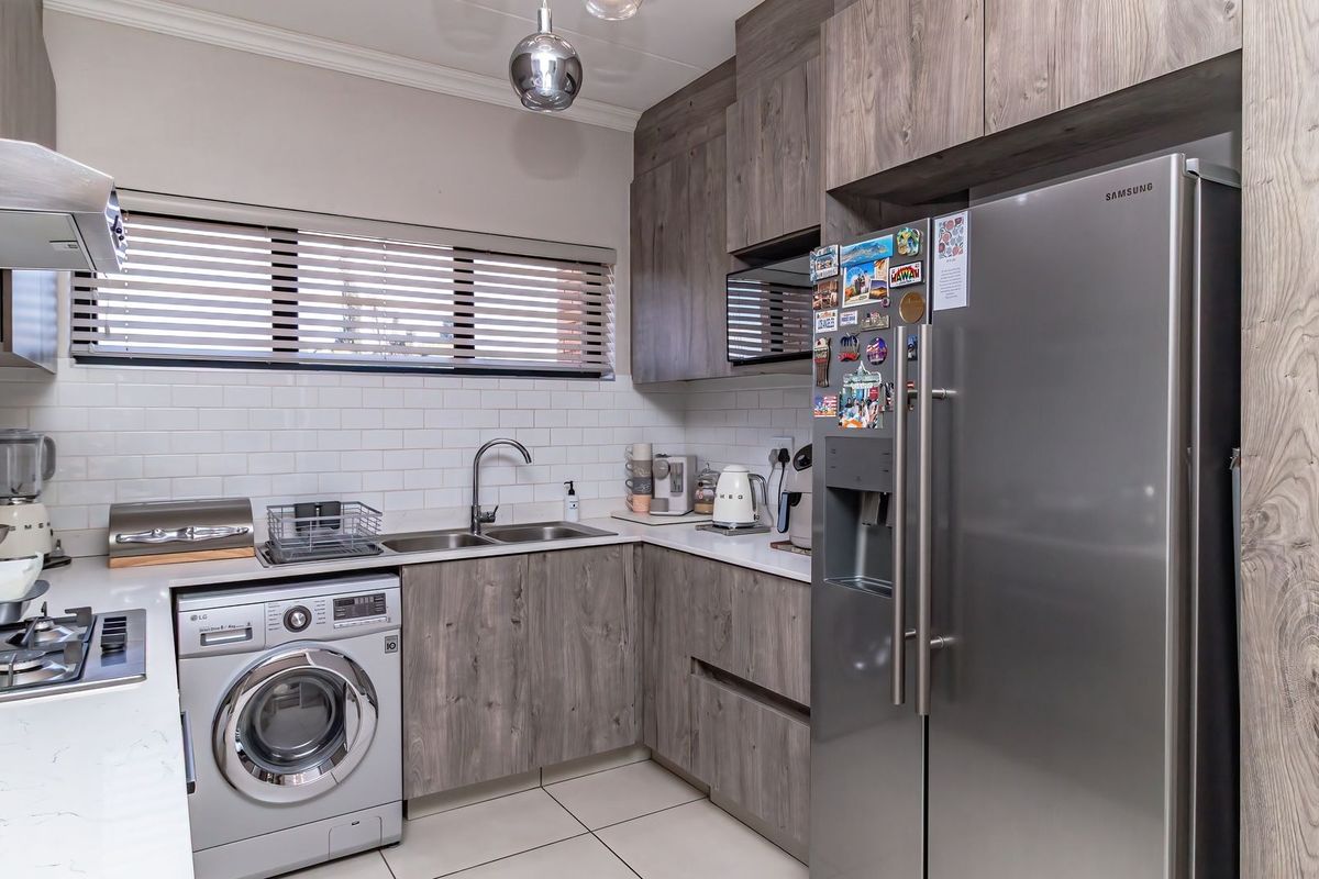Modern kitchen featuring wood-grain cabinetry, subway tile backsplash, gas hob with extractor, and integrated space for a washing machine.
