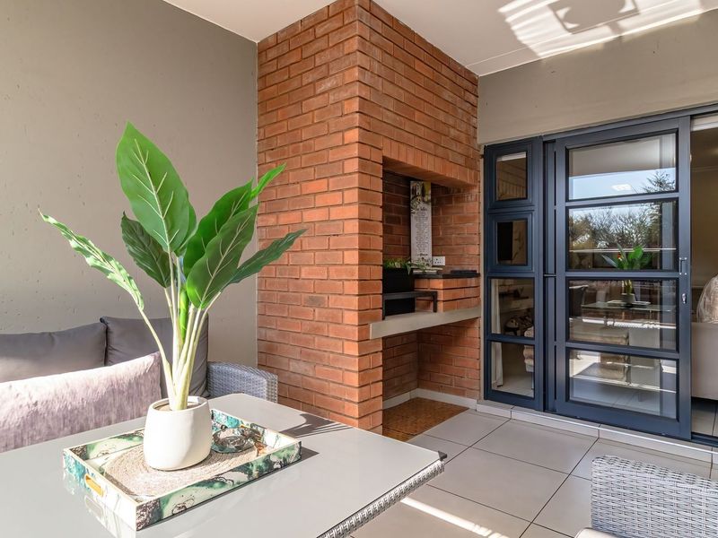 Covered patio featuring a built-in brick braai, tiled flooring, and modern aluminium sliding doors providing seamless access to the interior living space.
