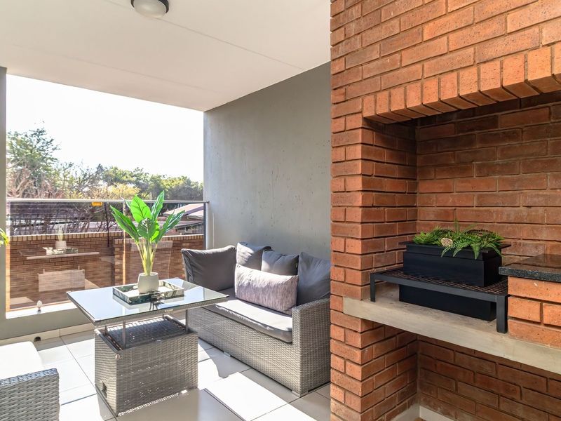 A covered balcony featuring a built-in brick braai with a granite prep surface and a modern glass balustrade overlooking the surroundings.