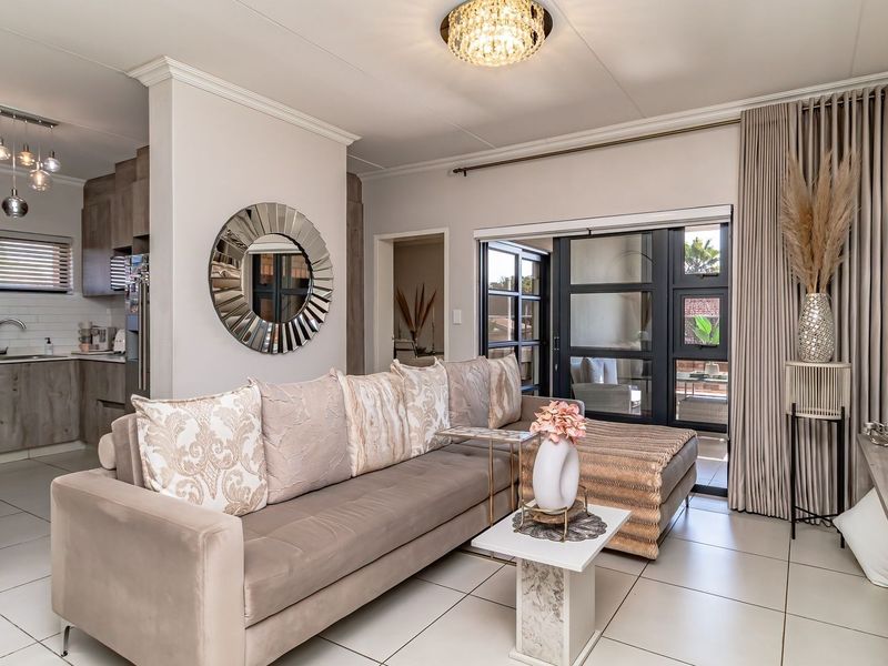 Modern open-plan living area featuring tiled floors, crown molding, and a seamless transition to a contemporary kitchen and outdoor patio space.