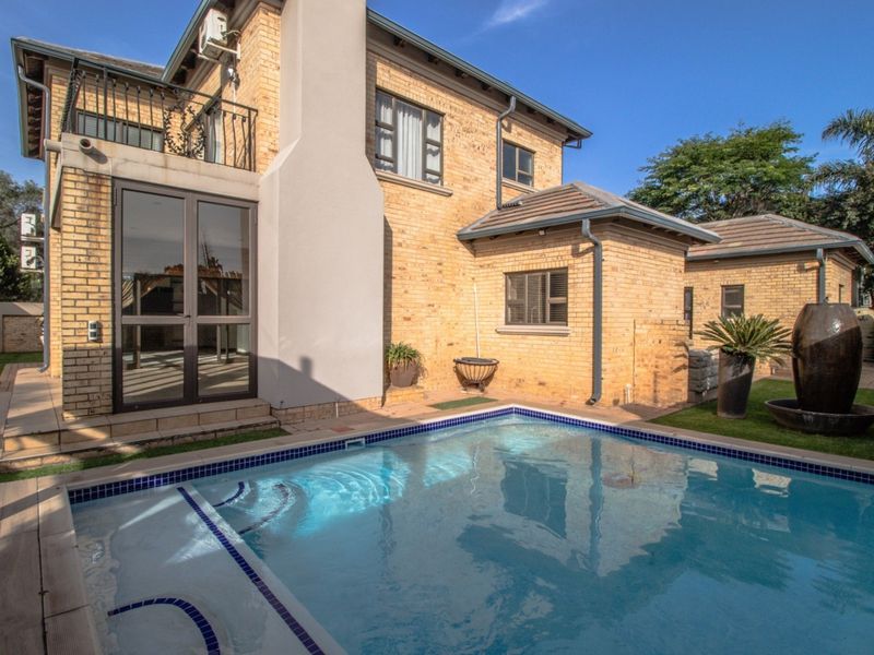 Rear view of the property featuring a well-maintained swimming pool, brick facade, and an upper-level balcony.