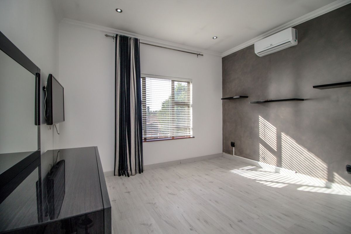 A bright, modern bedroom featuring light laminate flooring, a feature wall with floating shelves, and a wall-mounted air conditioning unit.