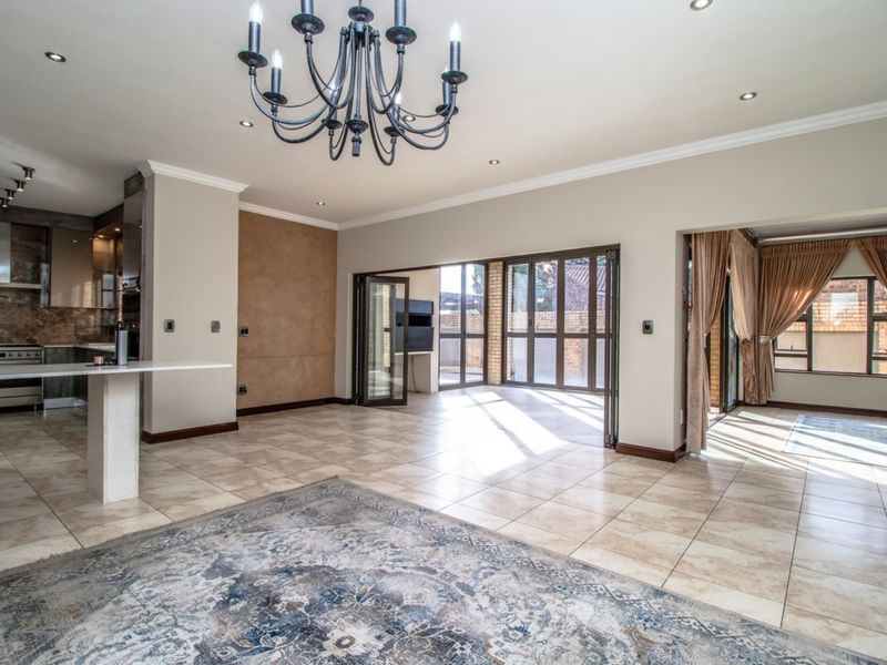 Spacious open-plan living area featuring tiled floors, a modern kitchen with stone island, and folding glass doors leading to an outdoor space.