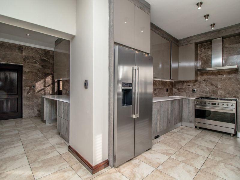 Modern kitchen featuring high-gloss cabinetry, stone countertops, marble-look wall tiles, and premium stainless steel appliances, including a gas stove and extractor fan.