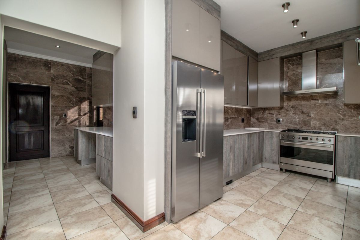 Modern kitchen featuring high-gloss cabinetry, stone countertops, marble-look wall tiles, and premium stainless steel appliances, including a gas stove and extractor fan.