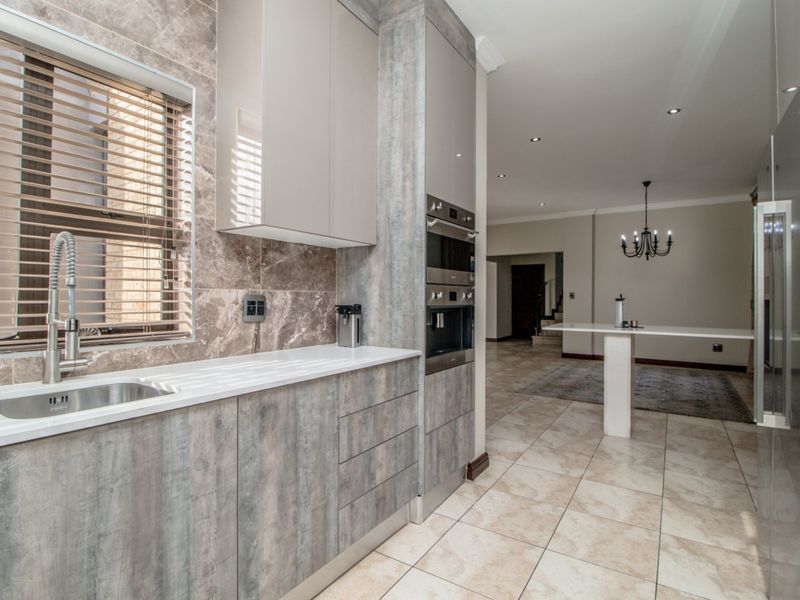 Modern kitchen featuring sleek wood-grain cabinetry, stone countertops, integrated appliances, and tiled flooring, flowing into an open-plan living area.