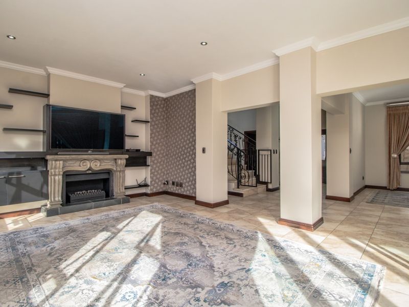 Spacious living room featuring a stone fireplace, built-in shelving, tiled flooring, and an open-plan layout leading to a staircase.
