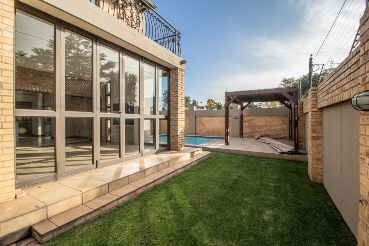 Rear garden area featuring a swimming pool, tiled patio with a wooden pergola, and direct access to the home via large aluminium sliding doors.