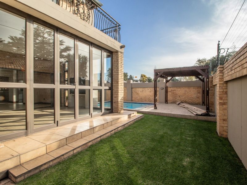 Rear garden area featuring a swimming pool, tiled patio with a wooden pergola, and direct access to the home via large aluminium sliding doors.