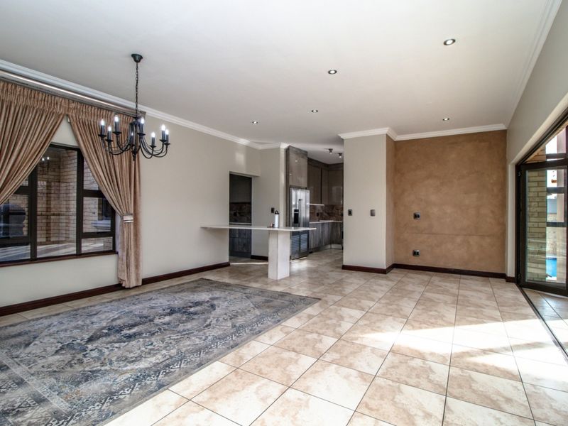 Spacious open-plan living and dining area featuring tiled floors, recessed lighting, and a breakfast bar, seamlessly connecting to the kitchen and outdoor patio.