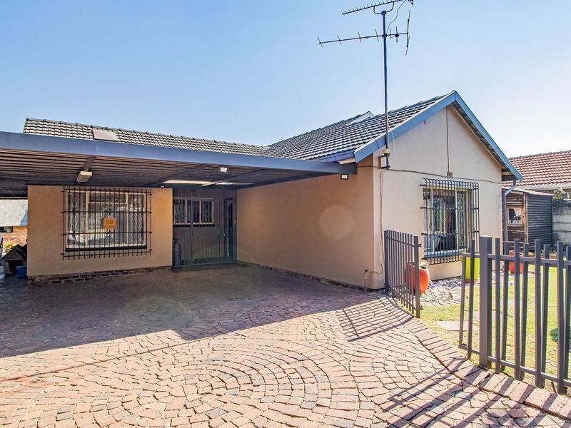 Front exterior view of the house featuring a paved driveway, a spacious carport, and secure metal fencing with security bars on the windows.