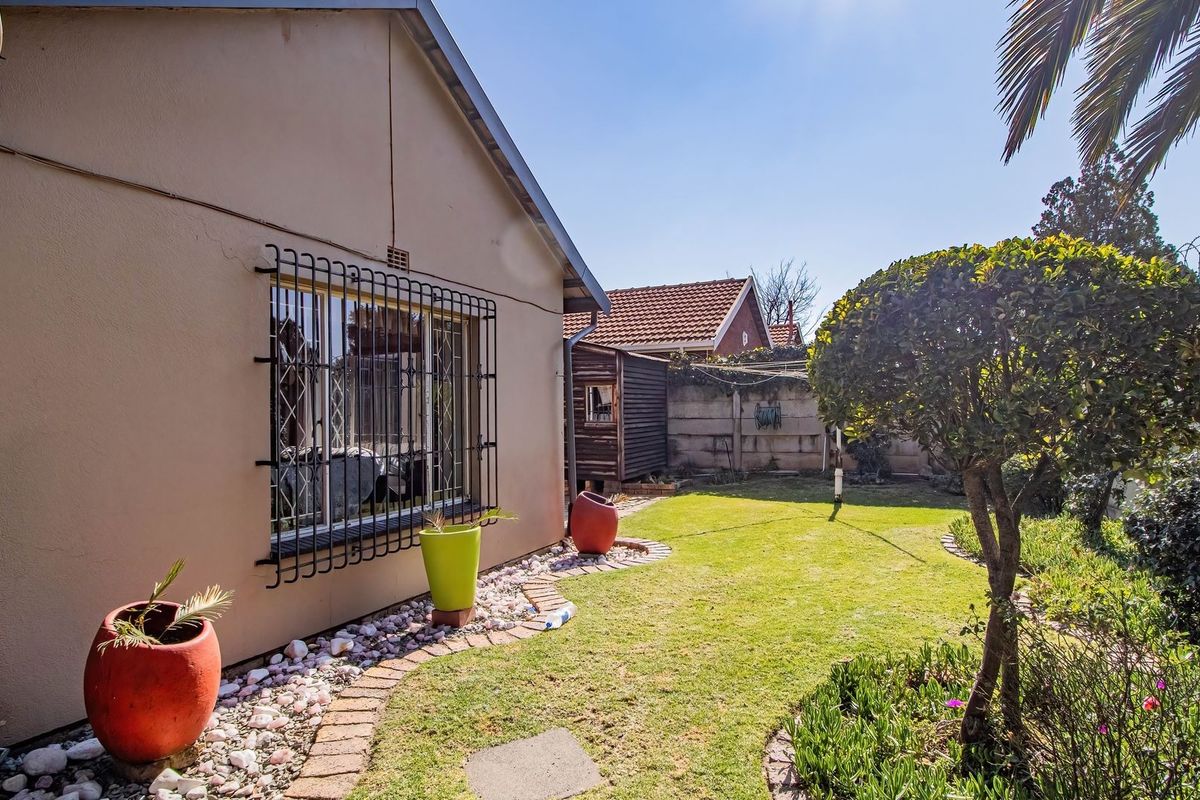 A view of the rear garden featuring a lawn, landscaped brick-edged borders, and security bars on the window of the main dwelling.