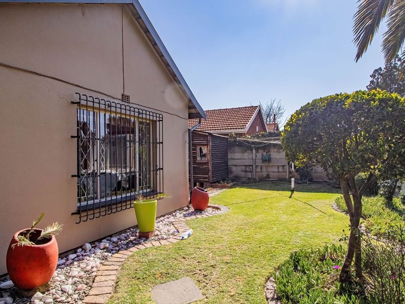A view of the rear garden featuring a lawn, landscaped brick-edged borders, and security bars on the window of the main dwelling.