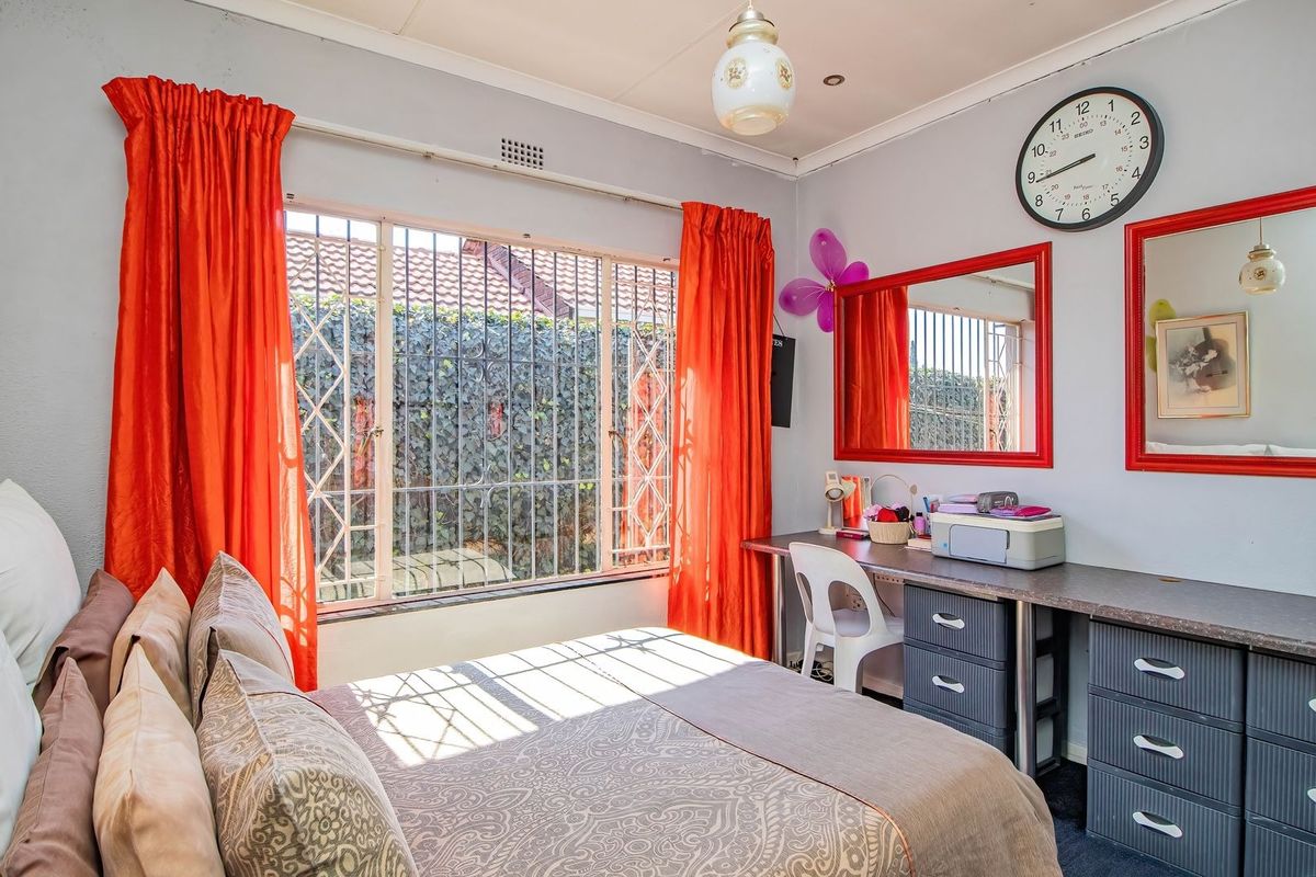 A functional bedroom featuring a built-in desk and storage unit, with a large window protected by a security gate.