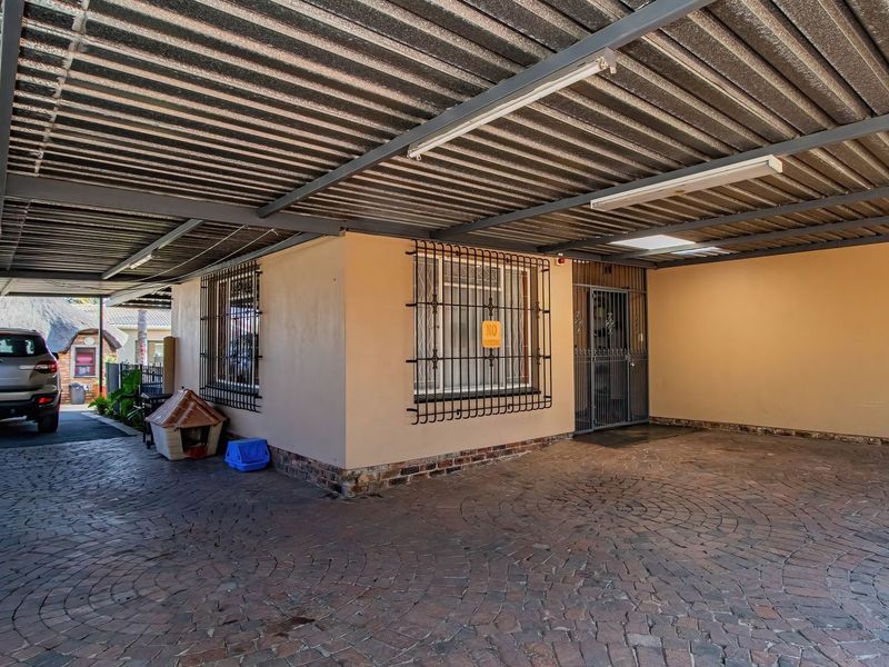 A spacious covered carport area featuring a corrugated metal roof, steel structural supports, and durable brick paving, providing secure off-street parking.