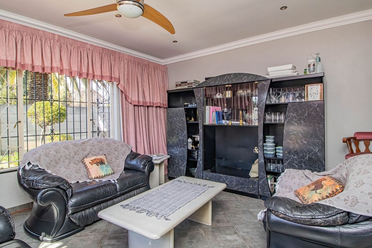 A living room featuring tiled flooring, a ceiling fan, and security bars on the windows, offering a functional space with classic architectural details.