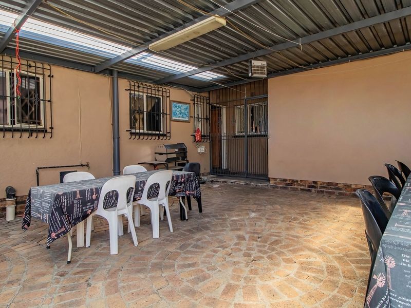 A covered outdoor patio area featuring brick paving, security window bars, and a corrugated metal roof, suitable for outdoor dining and entertainment.