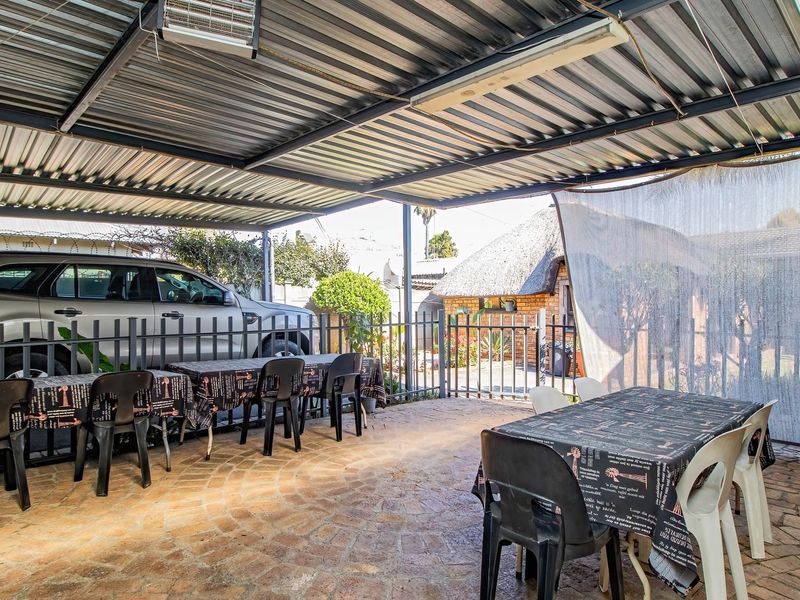 Covered outdoor patio area featuring a corrugated metal roof, brick paving, and metal fencing, suitable for outdoor entertaining.