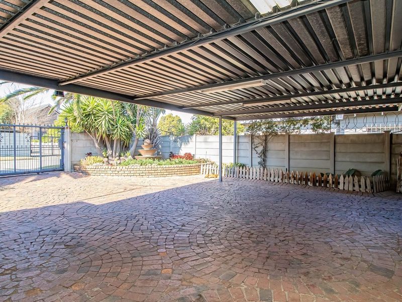 A spacious covered carport area featuring a paved driveway, perimeter walling, security gate, and a landscaped brick planter with a water feature.