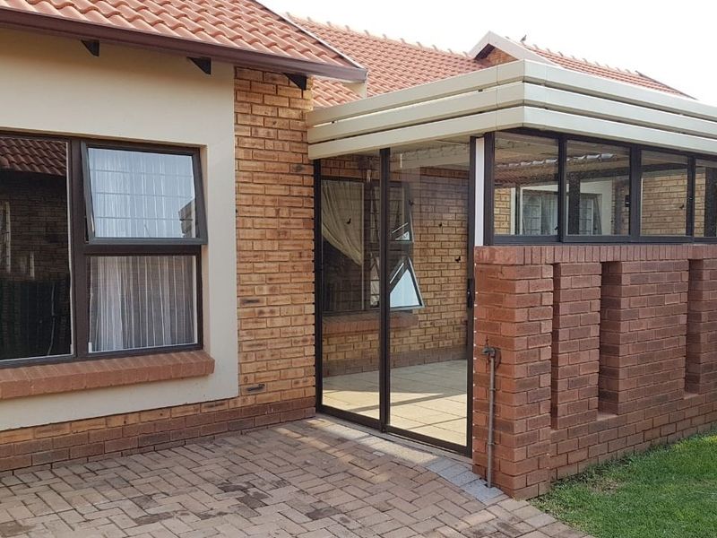 A well-maintained enclosed patio area featuring brick construction, paved flooring, and aluminium-framed sliding glass doors, providing a seamless transition to the garden.