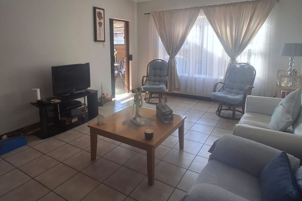 A comfortable living room featuring neutral tiled flooring and natural light through large windows, providing a functional and inviting space.