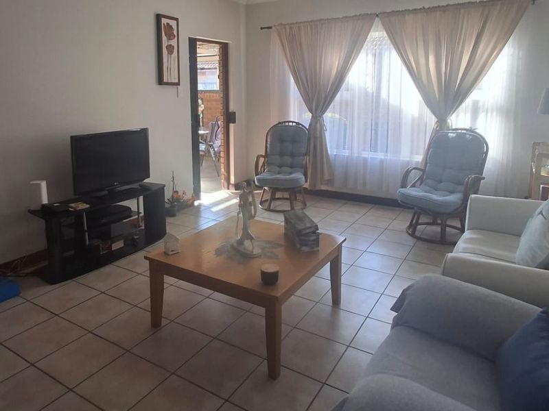 A comfortable living room featuring neutral tiled flooring and natural light through large windows, providing a functional and inviting space.