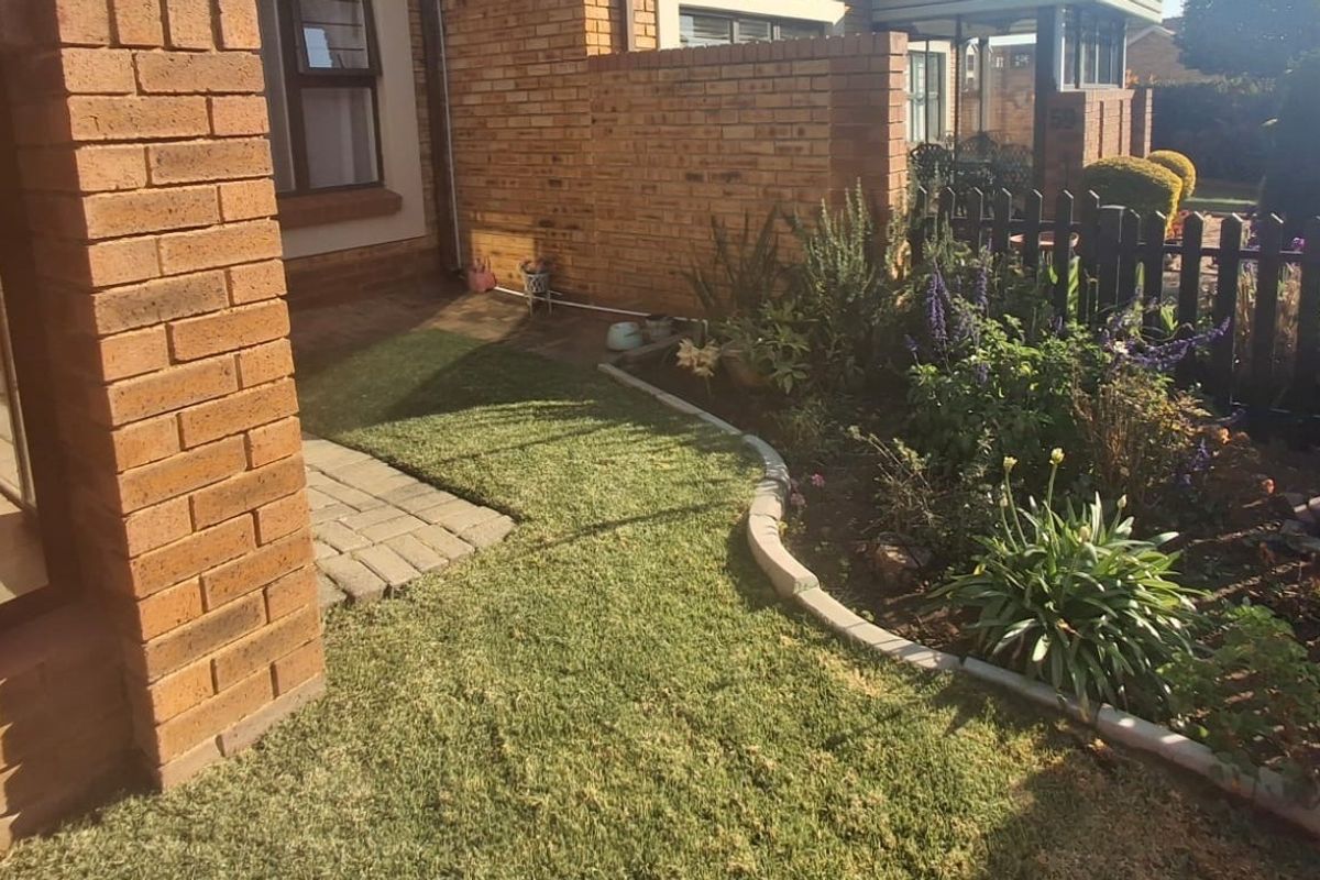 A well-maintained rear garden area featuring a paved walkway, face brick exterior walls, and established garden beds with concrete edging.