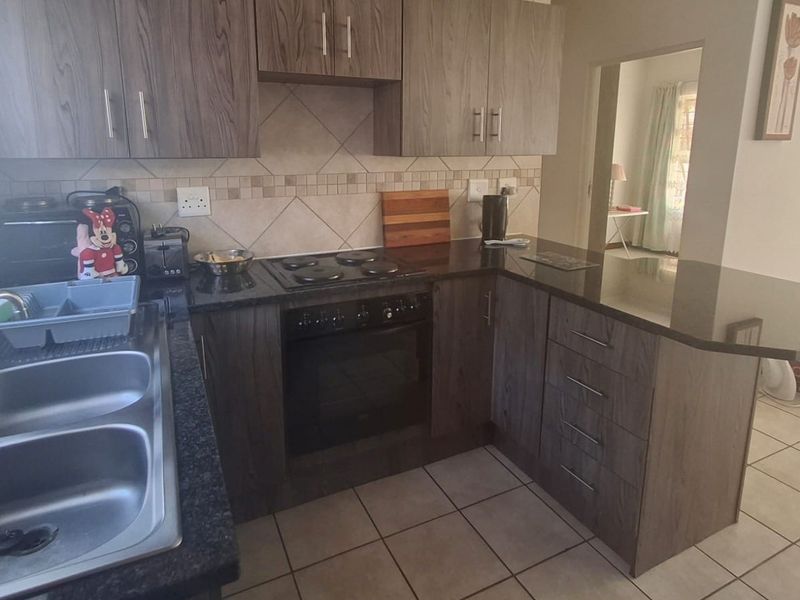 Functional kitchen featuring wood-look cabinetry, granite countertops, a breakfast bar, and integrated electric cooking appliances with a tiled backsplash.