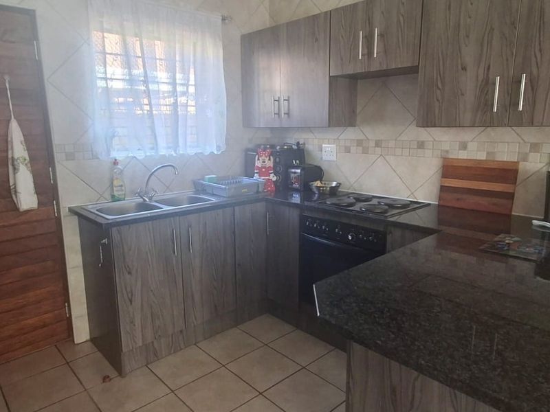 A functional kitchen featuring dark wood-look cabinetry, granite countertops, a built-in electric hob and oven, and tiled flooring.